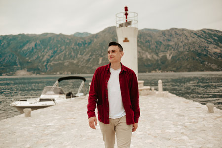 A man in a white T-shirt and red shirt walks on the island near the lighthouse. Travel, Montenegro.の写真素材