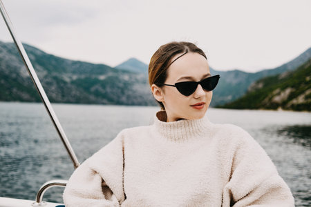 A girl in sunglasses and a white suit rides on a yacht. Journey to the mountains by sea. Travelingの写真素材