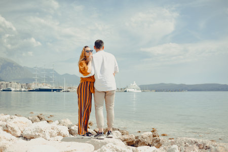 A couple walks along the beach against the backdrop of the sea and mountains. Travel of lovers. Love and honeymoon. Man and girl admiring natureの写真素材