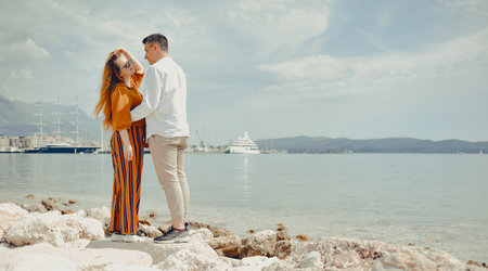A couple walks along the beach against the backdrop of the sea and mountains. Travel of lovers. Love and honeymoon. Man and girl admiring natureの写真素材