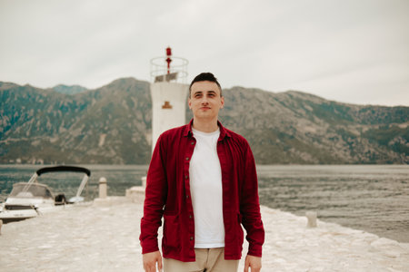 A man in a white T-shirt and red shirt walks on the island near the lighthouse. Travel, Montenegro.の写真素材