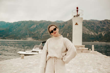 A stylish girl in a warm white suit walks on the island near the lighthouse. Travel, Montenegro.の写真素材