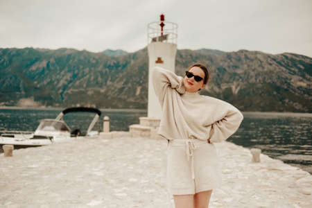 A stylish girl in a warm white suit walks on the island near the lighthouse. Travel, Montenegro.の写真素材