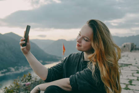 Woman on top of the mountain, view of the city and the sea. Girl holding smartphone, taking photo or video, selfie, travel bloggerの写真素材
