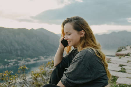 Woman on top of the mountain, view of the city and the sea. The girl holds a smartphone, calls on...