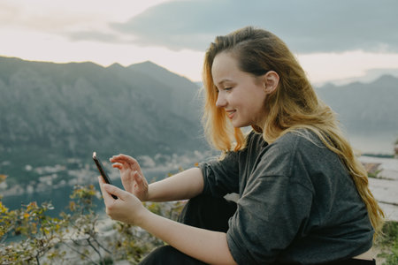Woman on top of a mountain in Montenegro, Kotor. The girl looks at the smartphone, writes something, printsの写真素材