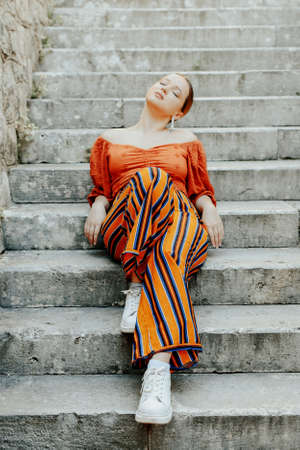 Gorgeous brunette posing lying on the stairs. Jewelry silver earrings, professional makeup, yellow...