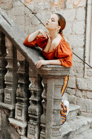 Gorgeous portrait of a beautiful woman in the old city on the stairs. Girl with makeup and hairstyle, long silver earrings posingの写真素材