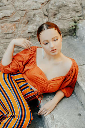 Gorgeous brunette posing lying on the stairs. Jewelry silver earrings, professional makeup, yellow...