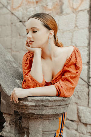 Gorgeous portrait of a beautiful woman in the old city on the stairs. Girl with makeup and hairstyle, long silver earrings posingの写真素材
