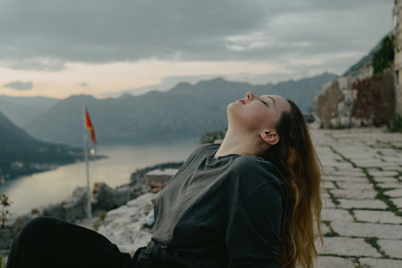 Woman on top of the mountain, view of the city and the sea. The girl looks at pleasure, breathes air, closed her eyes, a place of powerの写真素材