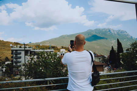 A man against the backdrop of mountains and flowers on a sunny day, a tourist takes a photoの写真素材