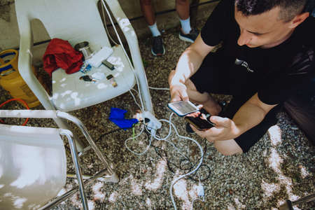 A man charges his phone outdoors at a campsite. Tourist and a lot of wires for charging. Where to charge in a tent or travelの写真素材