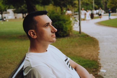A man sits on a bench and looks up. The guy thinks sitting in a green parkの写真素材