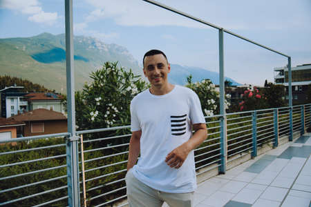A man against the backdrop of mountains and flowers on a sunny day tourist smiles and rests in Italy. hipster photoの写真素材