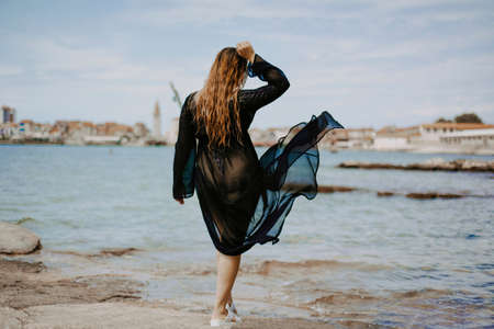 A woman with a flying pareo. Gorgeous brunette on the beach against the backdrop of the sea and the European city.の写真素材