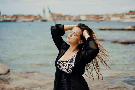 Gorgeous brunette on the beach against the backdrop of the sea and the European city. Vacation in summer, beautiful brunette. atmospheric portraitの写真素材