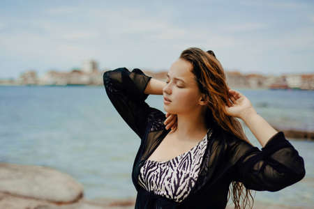 Gorgeous brunette on the beach against the backdrop of the sea and the European city. Vacation in summer, beautiful brunette. atmospheric portraitの写真素材