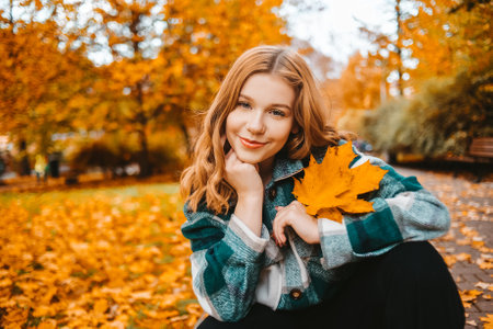A woman is sitting in an autumn park. Girl teenager on a background of autumn leaves. Fashion photo Looking at the camera smilingの写真素材