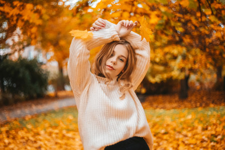 Photo portrait of a girl in a white sweater, the blonde holds leaves in her hands. Pretty woman in the park in autumn. Autumn fashion and style. Warm moodの写真素材
