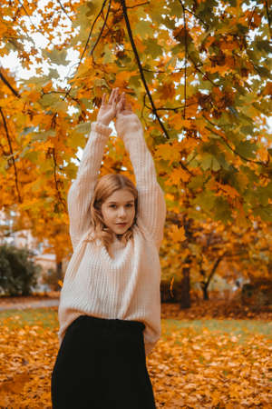 A girl in a white sweater stands in an autumn park and poses. Teenagerの写真素材