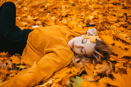 A beautiful girl lies in autumn leaves in the park, gorgeous hair, a teenager rests in autumnの写真素材