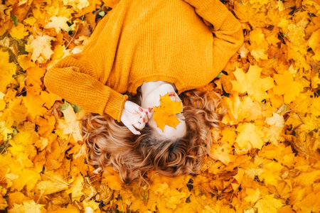 Beautiful girl lies in the park in autumn. A teenager in a yellow sweater on a background of orange...
