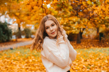 Photo portrait of a girl in a white sweater, beautiful brunette. Pretty woman in the park in autumn laughs, joy, smile. Autumn fashion and styleの写真素材