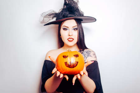 A witch girl holds a pumpkin in her hands and stretches out to the camera, a woman celebrates Halloween, photo on a white backgroundの写真素材