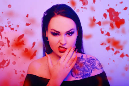 Brunette in neon with a tattoo and red lips. Woman halloween party, blood runs down her face, professional make-up for a partyの写真素材