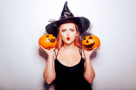 Beautiful girl witch is holding a pumpkin in her hands. Woman celebrating halloween, joy and a smile on her face. Autumn holidays and partiesの写真素材