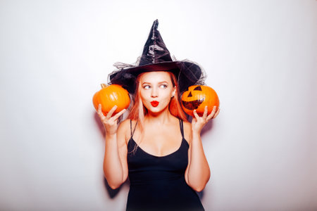 The witch listens to the pumpkins, the model is shocked. Woman with hat and black dress, halloween party.の写真素材