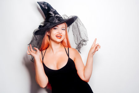 Pink-haired woman witch, in a hat on a white background, halloween costume. The girl smiles and looks to the side at the empty space. Halloween partyの写真素材