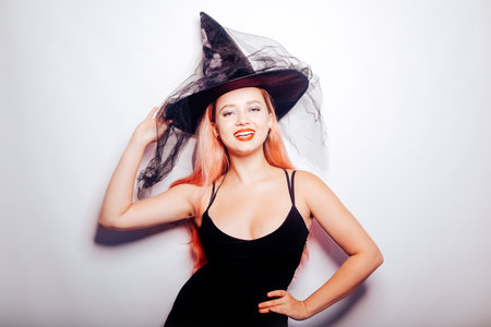 Pink-haired woman witch, in a hat on a white background, halloween costume. The girl smiles and looks to the side at the empty space. Halloween partyの写真素材