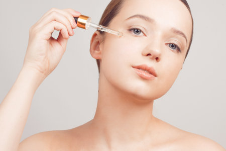 Girl on a white background skin care, oil, serum with a pipette on her faceの写真素材