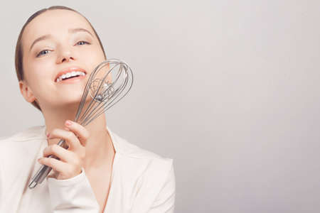 The girl chef holds a whisk and poses with him on a white background. cooking schoolの写真素材