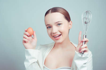 Chef girl, school of chefs in white background, balloon whisk and aggs and cooks, cooking courses, school cooks. The girl grimaces, shows emotions.の写真素材