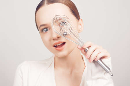 The girl chef holds a whisk and poses with him on a white background. cooking schoolの写真素材
