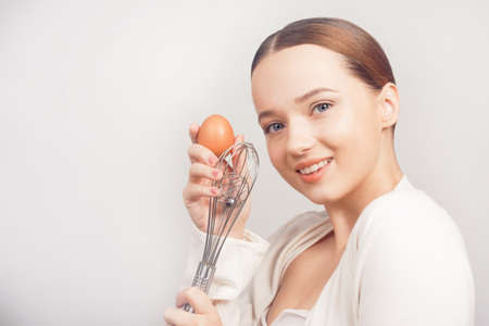 Chef girl, school of chefs in white background, balloon whisk and aggs and cooks, cooking courses, school cooks. The girl grimaces, shows emotions.の写真素材