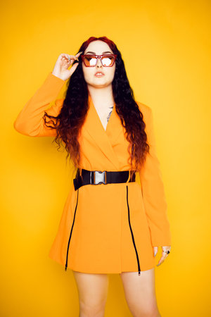 Brunette in red glasses on an orange background in a dress jacket. Fashion photo of model in sunglasses.の写真素材