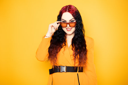 Brunette in red glasses on an orange background in a dress jacket. Fashion photo of model in sunglasses portraitの写真素材
