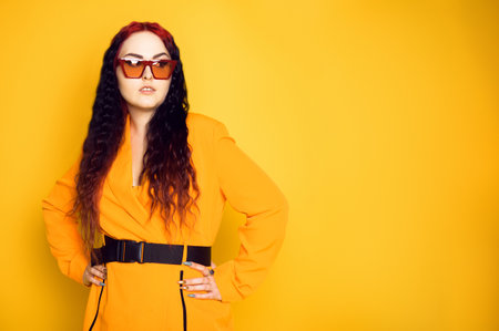 Brunette in red glasses on an orange background in a dress jacket. Fashion photo of model in sunglasses.の写真素材