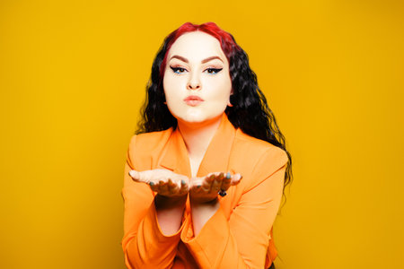 A beautiful brunette with red hair and an orange cloak on a yellow background sends air kisses