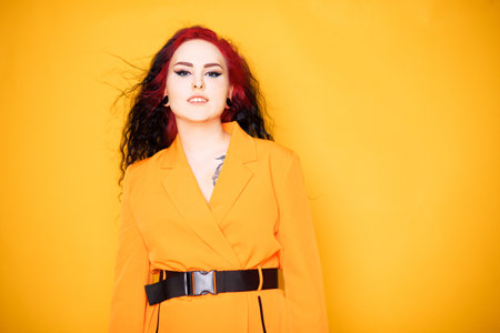 Beautiful girl on a yellow background. A brunette in an orange dress and long hair is posing, smiling, having fun. Summer photo woman in studio. Joy and emotion. Red hair roots place for textの写真素材