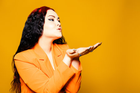A beautiful brunette with red hair and an orange cloak on a yellow background sends air kissesの写真素材