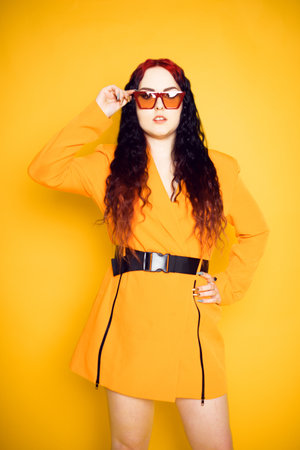 Brunette in red glasses on an orange background in a dress jacket. Fashion photo of model in sunglasses.の写真素材