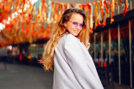 Fashion photo of a beautiful fashionable girl at the festival on the background of confetti. Stylish purple jacket and glasses.の写真素材