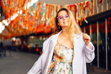 Fashion photo of a beautiful fashionable girl at the festival on the background of confetti. Stylish purple jacket and glasses.の写真素材