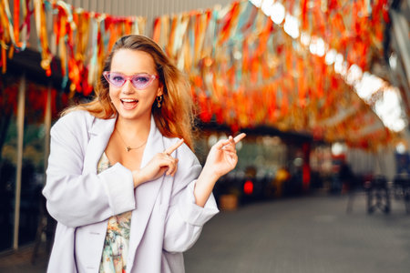 A girl in a dress, jacket and purple sunglasses poses at the festival. Woman showing her hand to the side, space for text or productの写真素材