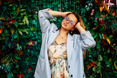 A girl in a dress, jacket and purple sunglasses poses at the festival portrait. Smile and joy, emotions against the backdrop of greenery and a waterfall. fashion outfitの写真素材